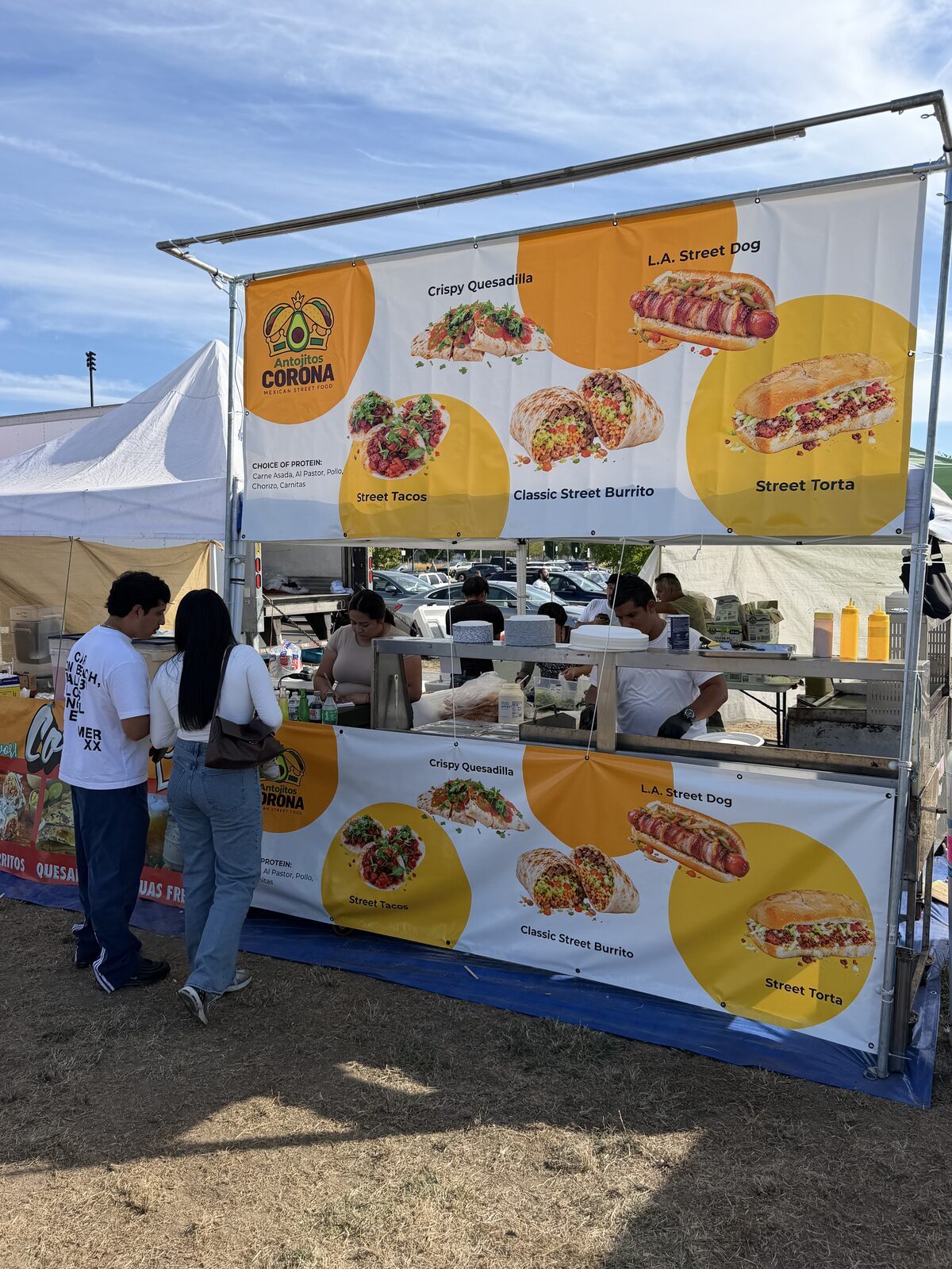 Puesto de Antojitos Corona en un evento al aire libre, con los banners del menú sobre el mostrador