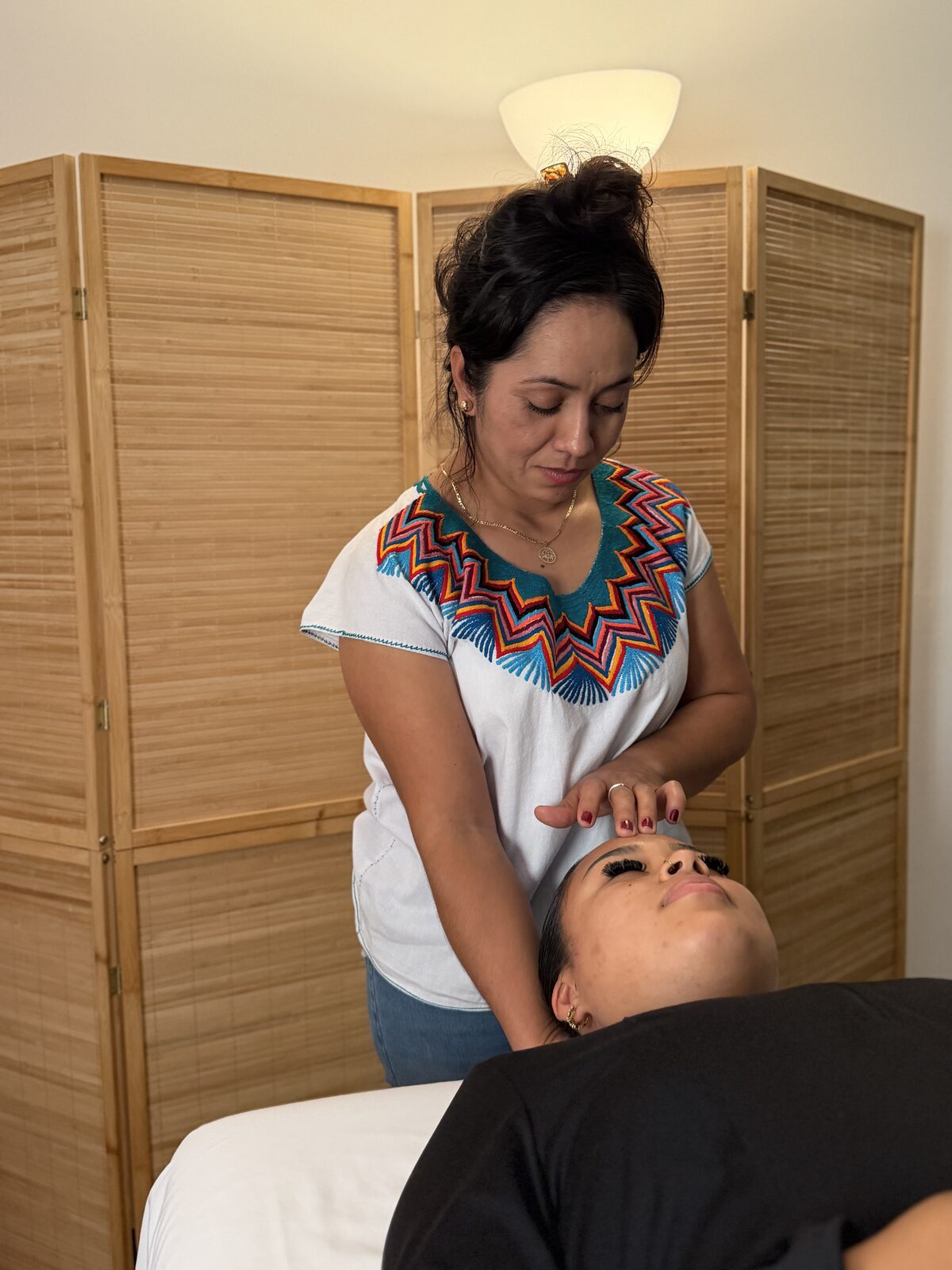 Una terapeuta con la mano sobre la frente de una persona recostada, dentro de la sala de masaje de Casa Latido